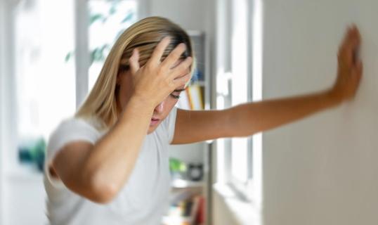 Person with hand on their head, leaning against wall, with the room spinning