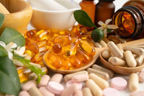 Pills of different sizes, shapes and colors are surrounded by bottles, mortars and pestles, and plants