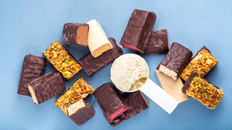 A selection of different protein bars surround a scoop of protein powder.