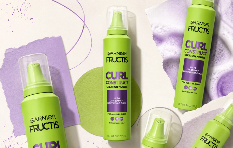 A lime-green Garnier Fructis Curl Construct Creation Mousse bottle appears in an editorial-style collage with multiple cropped product cutouts, lavender paper textures, purple graphic accents and soft studio shadows on a cream background