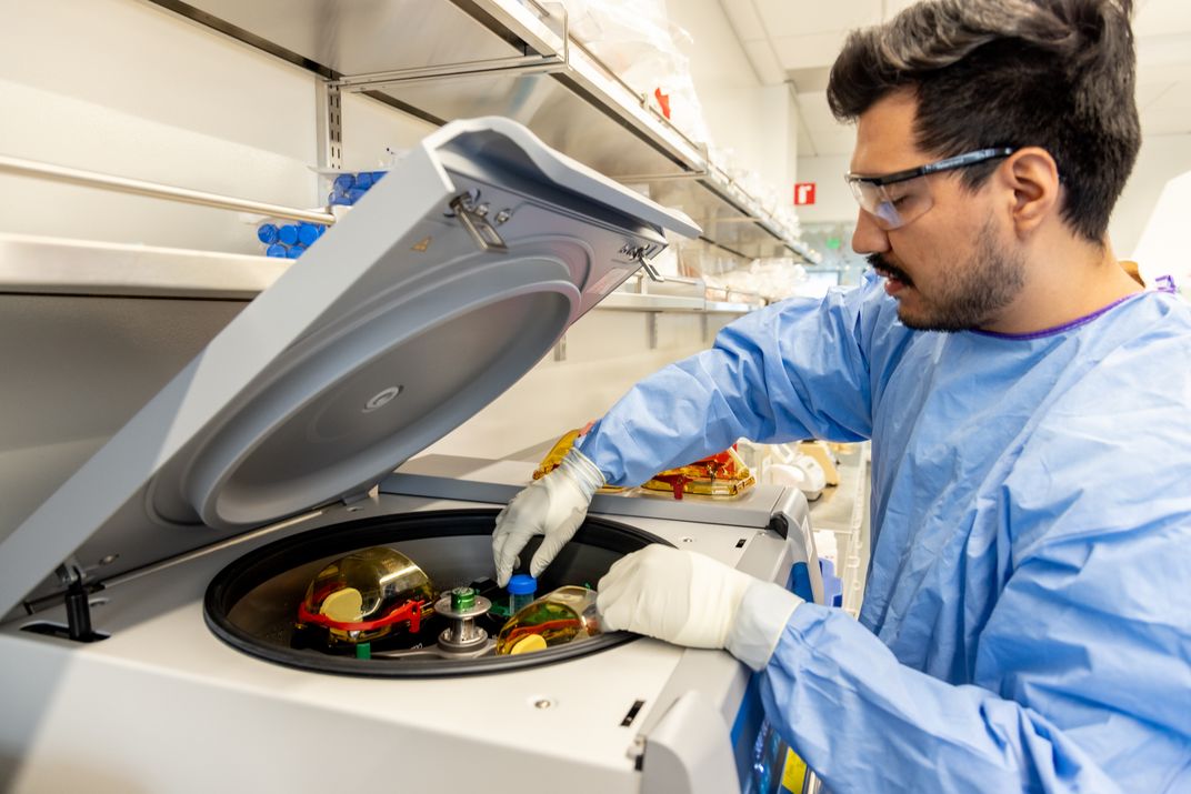 Emmanuel Velazquez places a cerebrospinal fluid sample into a centrifuge for processing