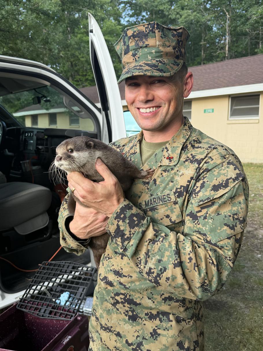 A Marine in uniform smiles while holding an otter.