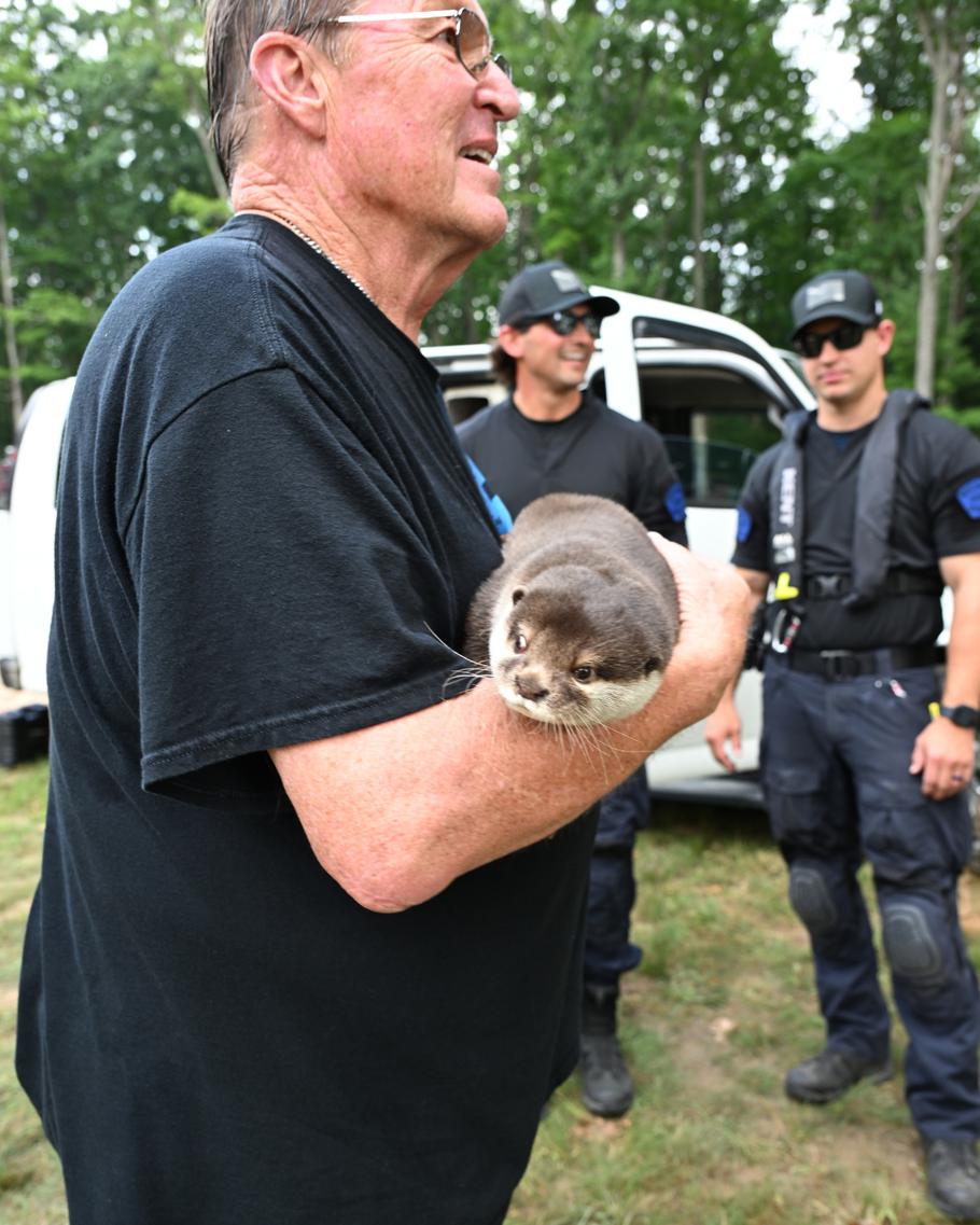 A man holds an otter as three people in tactical gear stand nearby.