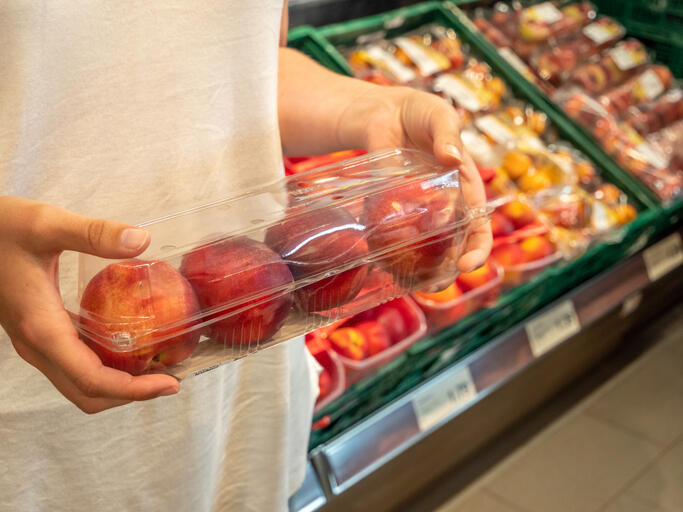 Person holding four peaches in a plastic container in a grocery store.