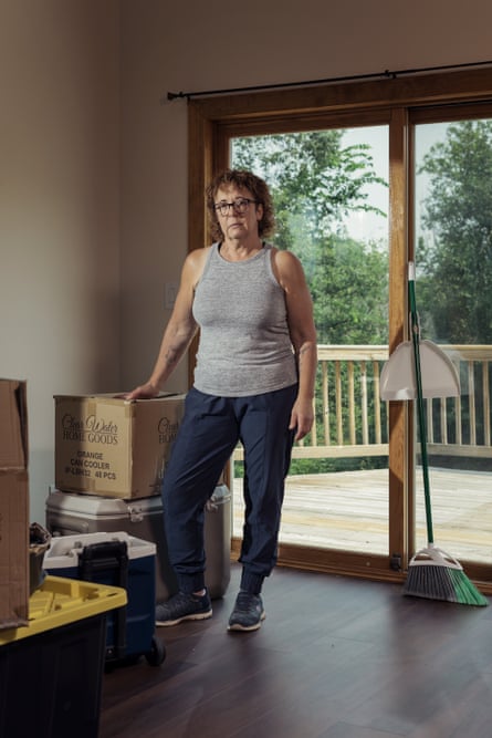 Woman stands in room bare except for stacked boxes and a broom.