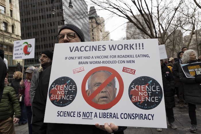 Someone with a poster that says "Vaccines work!!! If only we had a vaccine for roadkill eating, brain-worm-riddled con men."