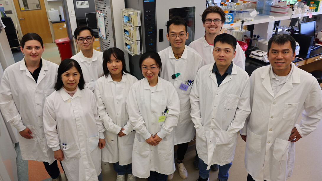 Nine scientists in white labcoats pose for a group photo in a lab.