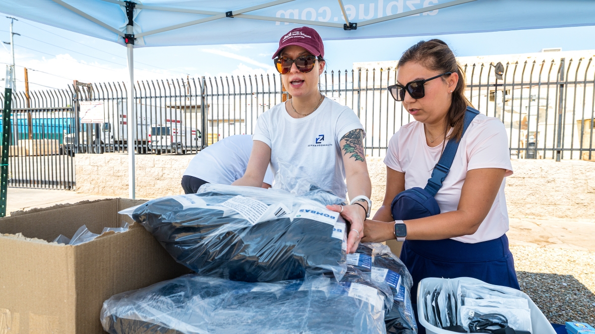 Two women stand at a table and take supplies out of boxes.