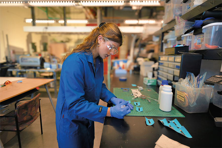Woman in blue jumpsuit working on blue marker sensors.
