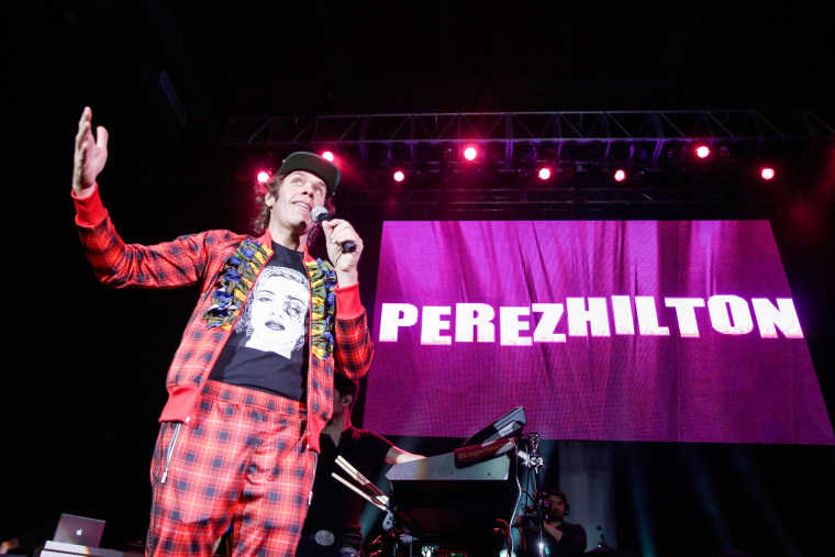 Perez Hilton speaks on stage, a screen behind him reads "Perez Hilton" in white text on a pink background