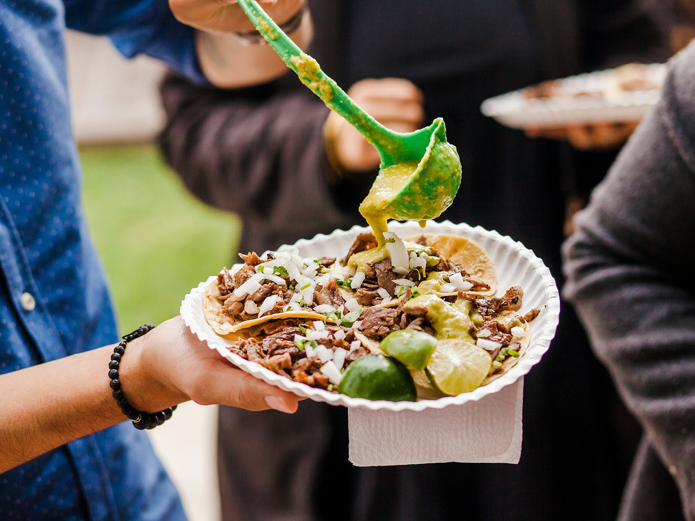 A photo of a person ladeling sauce on a plate of meaty tacos