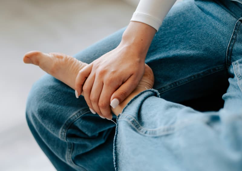 A person with their foot across their thigh, rubbing their ankle.