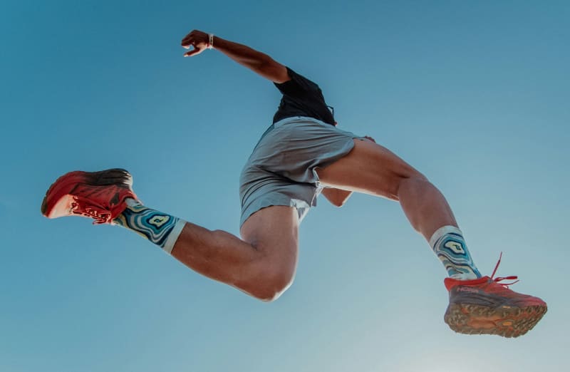 A runner is seen midstride from below with a blue skhy above.