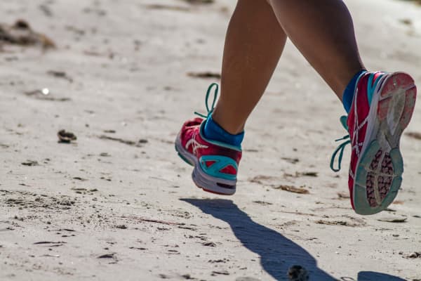 A pair of legs in running shoes move along a beach.