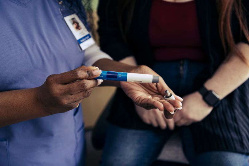 Close-up of nurse's hands holding a medical pen-like device for self-injection. Proper technique is essential for safe medication administration.