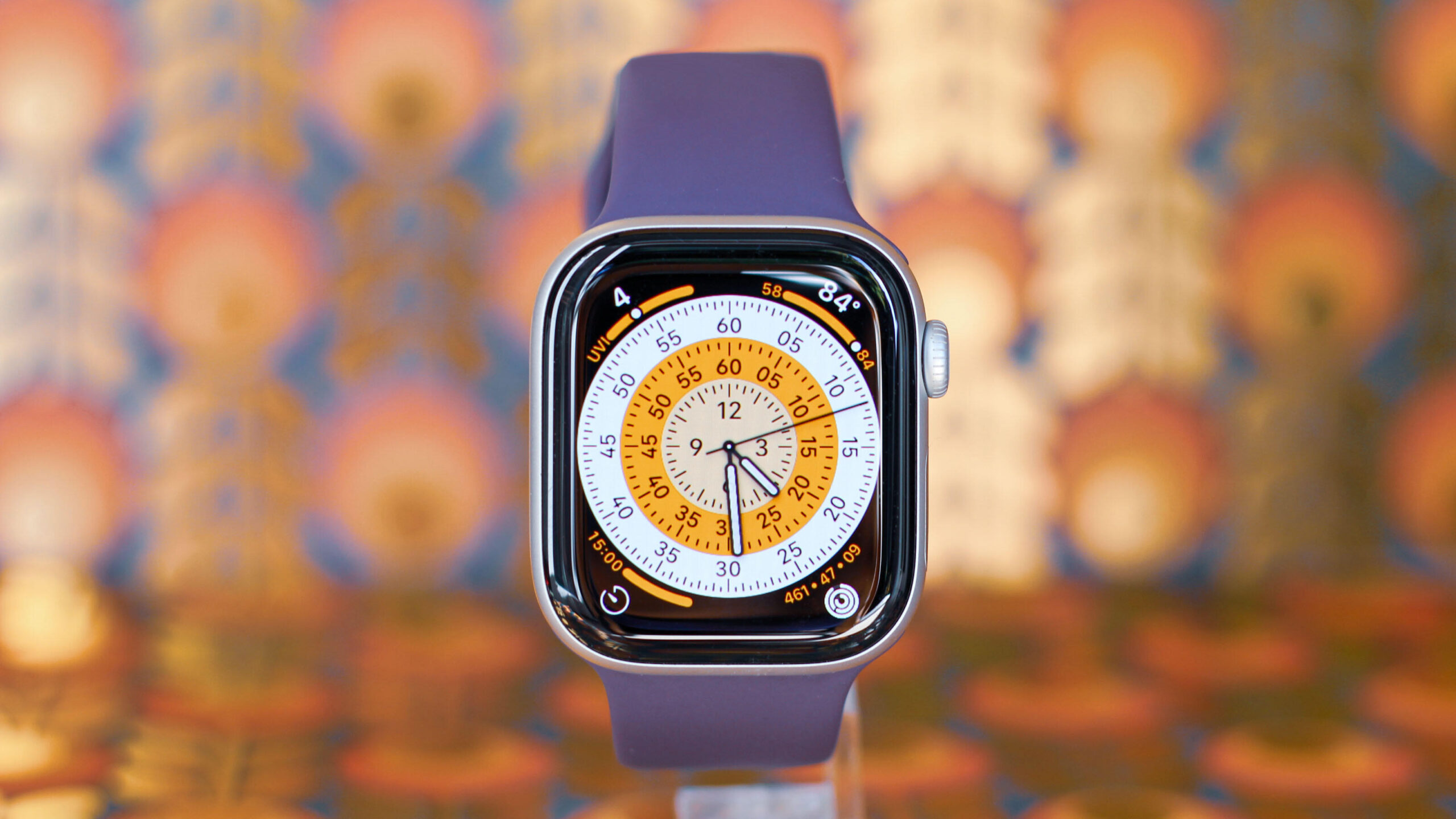 An Apple Watch Series 11 with purple band on a blurred, colorful background.