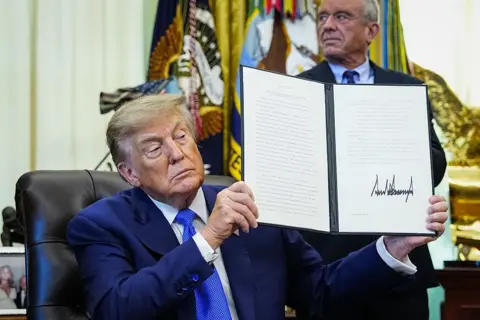Getty Images US President Donald Trump holds up an executive order he signed that aims to change childhood vaccine administration