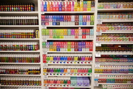 Shelves of various flavoured disposable vapes and e-liquids in a vape shop. They are in brightly coloured packets.