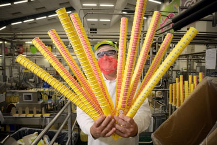 A worker in a n ice-cream factory, wearing a face mask and holding lots of cardboard ice-cream holders