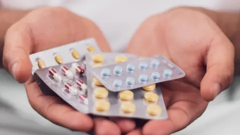 Getty Images A hand holding a series of pharmaceutical drugs in packets.