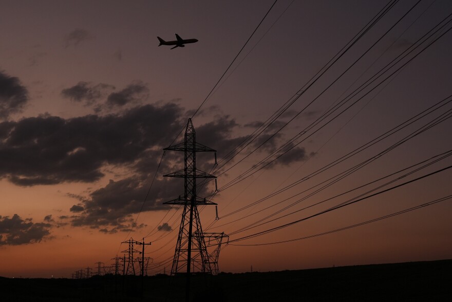 A plane passes over power lines at dusk in San Antonio, Monday, Aug. 3, 2026. (AP Photo/Eric Gay)