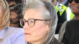 Woman with grey hair wearing black glasses and brown blazer