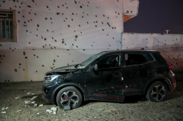A damaged car sits beside a wall bearing numerous impact marks near the site of a strike in Lamerd, southern Iran, Saturday, Feb. 28, 2026. (Alireza Ameri/Tasnim News Agency via AP)