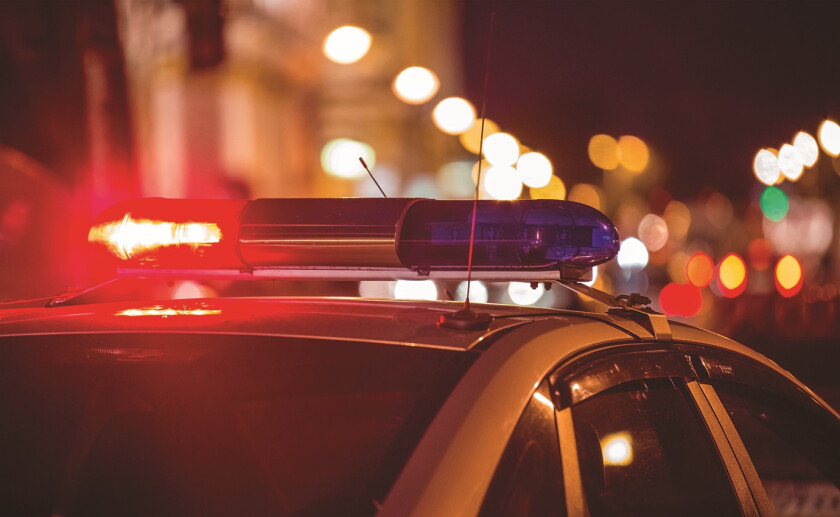 Stock art of red and blue emergency lights atop a police vehicle with the lights of a city street blurred in the background.