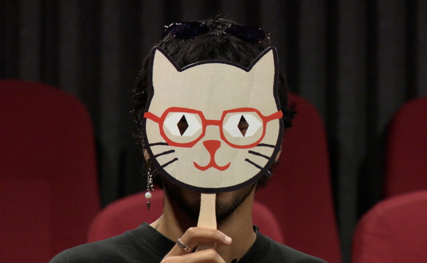 Kristian Perez-Franco is shown holding a cat mask/fan up to his face at Digital Gym Cinema on August 6, 2026. The fans will be handed out to audiences as long as supplies last.
