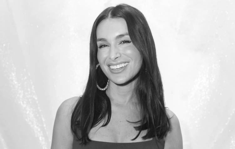 Ashley Iaconetti smiling widely, with long dark hair worn down and large hoop earrings.