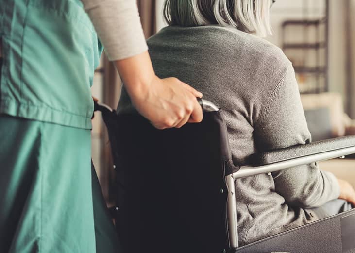 A home care nurse assisting an elderly patient in a wheelchair.