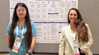 Yutong Chen and Ana Lopes pose in front of a poster at the conference