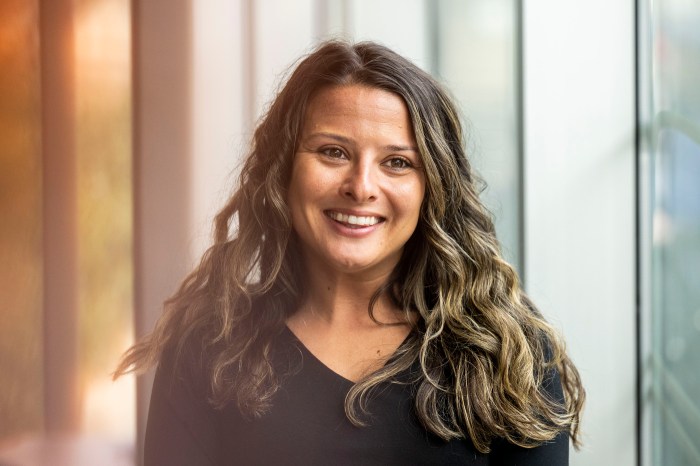 Ashleigh Shields smiling, wearing a black v-neck top, with a window and warm natural light in the background.