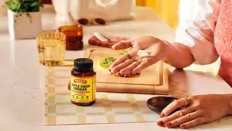 Hand holding Bragg apple cider vinegar capsules over an avocado toast board