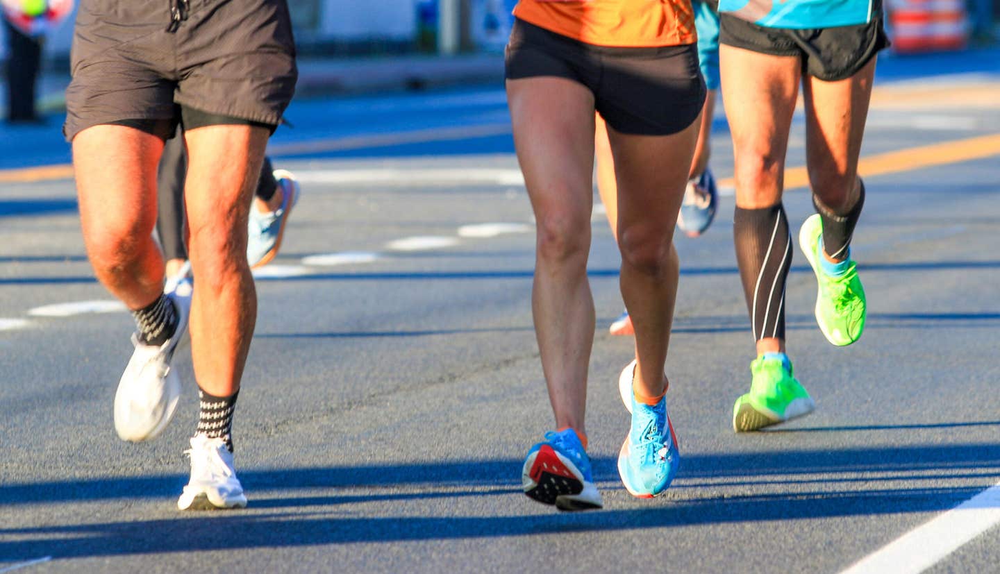Front view of the Legs of runners running a race on the roads in morning sunshine.