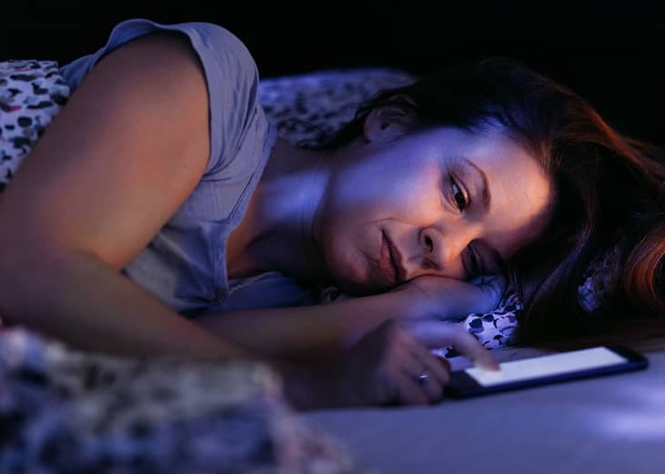 A stressed woman struggling to keep up with phone at night.
