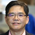 Wu has short black hair, eye glasses, and a black suit jacket over a red/white dress shirt.