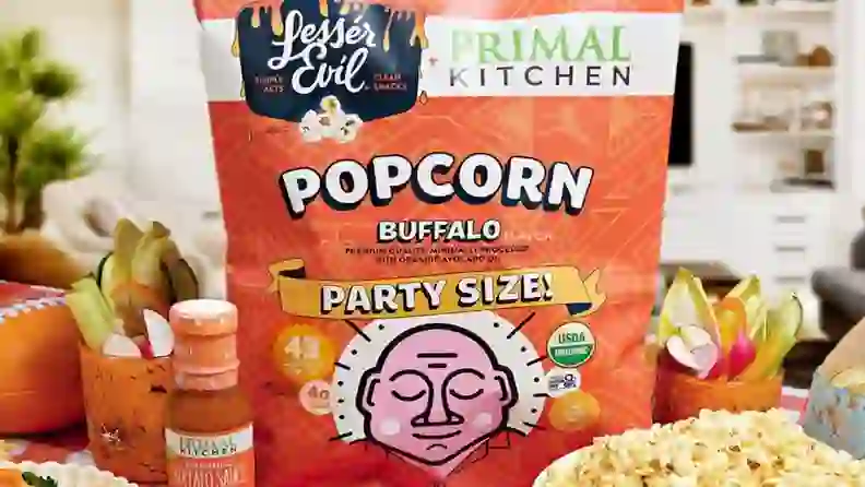 LesserEvil buffalo popcorn bag beside Primal Kitchen buffalo sauce and veggies