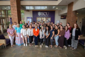 A large group of women and men pose for a photo in a building lobby.
