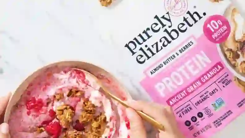 Purely Elizabeth protein granola bag beside a bowl of yogurt and berries