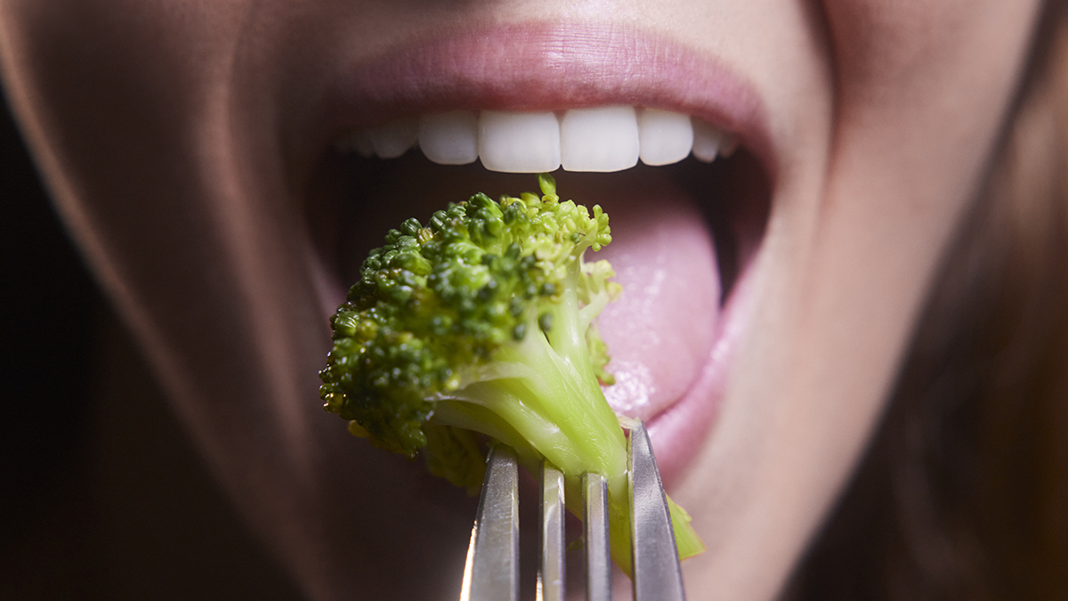 Young woman mouth eating broccoli