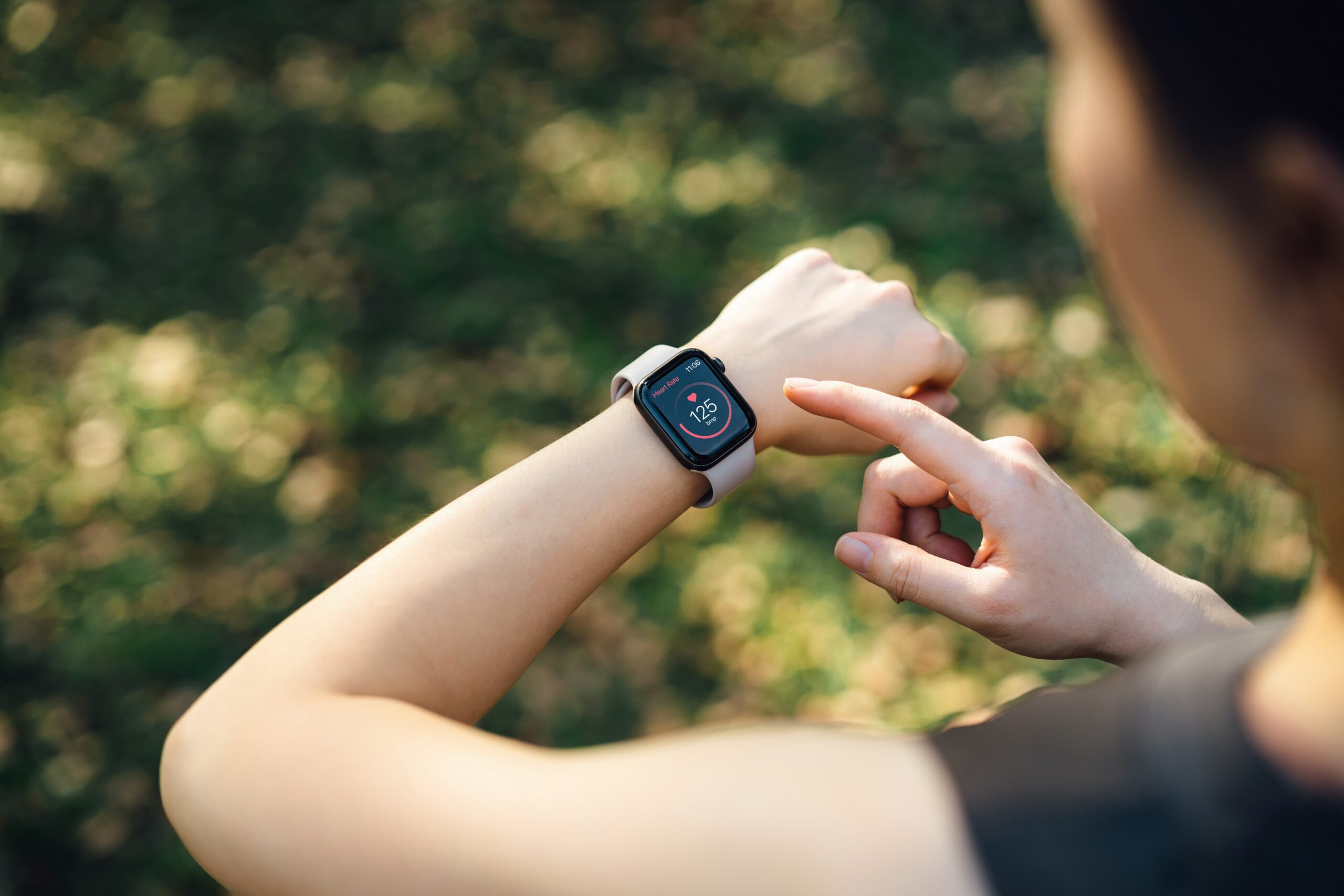 Person checking a smartwatch displaying health data, such as steps and heart rate, on their wrist outdoors