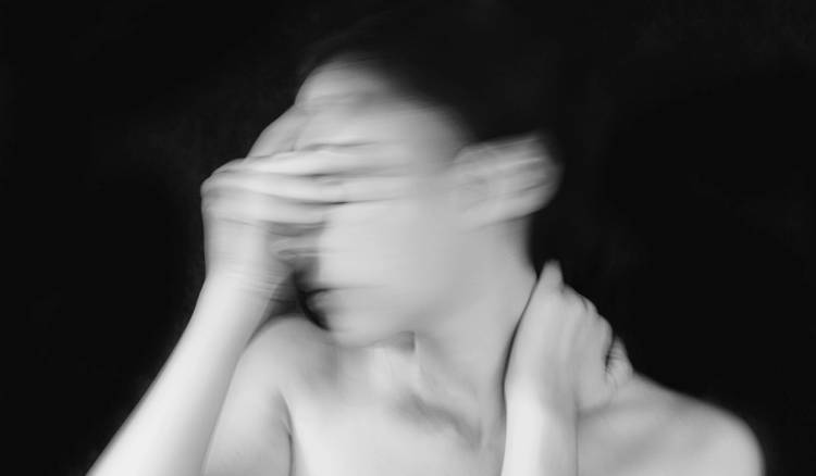 Black-and-white motion-blur portrait of a woman with her hand to her face against a dark background
