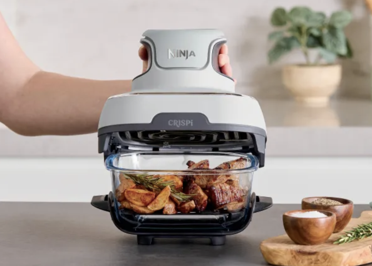 Hand holding cooking lid above glass-bowl air fryer