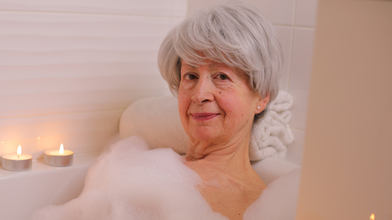 Senior woman taking a bath with candles and foam all around her