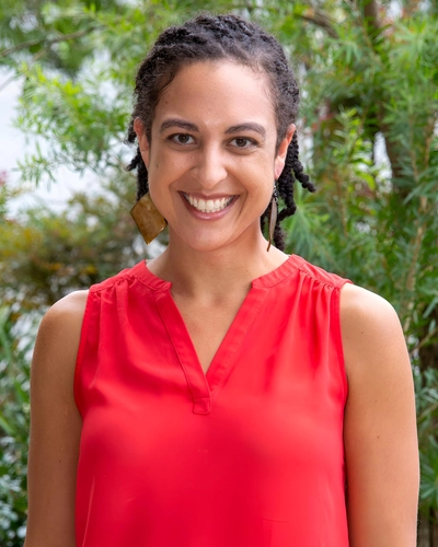 Portrait of Dr. Krista Mehari smiling outdoors in a bright sleeveless coral blouse.