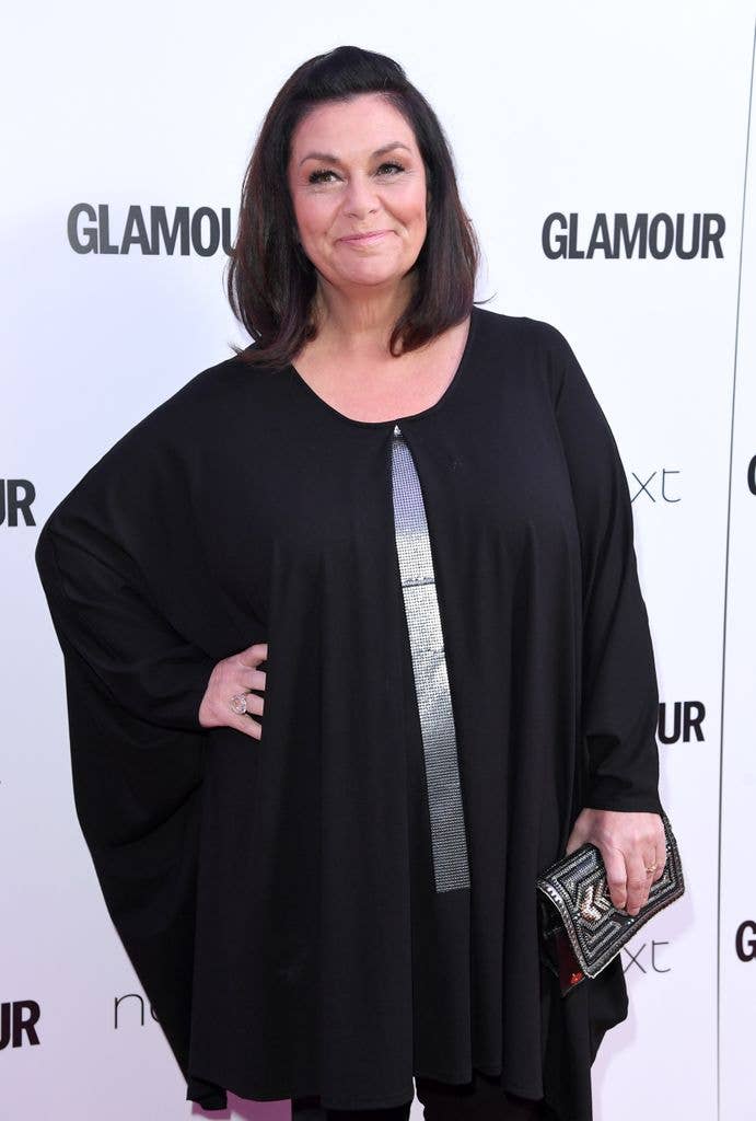Dawn French smiling, wearing a black dress with a silver stripe, holding a clutch