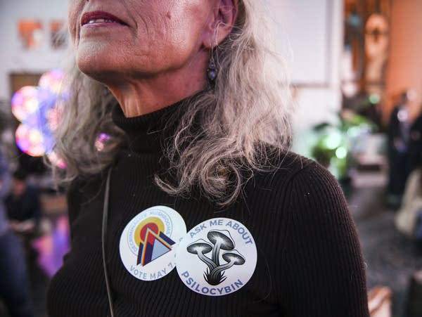 A person wears a sticker that says "ask me about psilocybin."