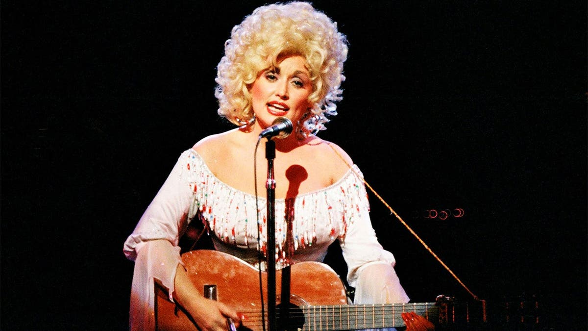 Dolly Parton plays guitar in 1983.