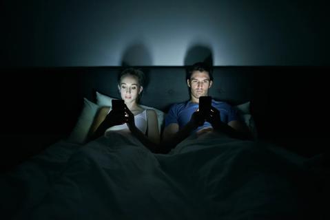 Couple sitting up in bed on their smartphones